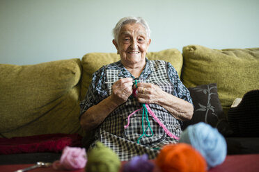 Portrait of smiling senior woman crocheting on the couch at home - RAEF02131