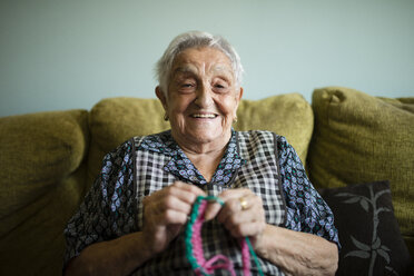 Porträt einer lächelnden älteren Frau, die zu Hause auf der Couch häkelt - RAEF02132