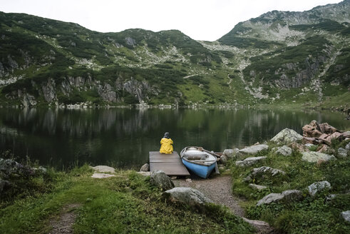 Austria, Tyrol, Fieberbrunn, Wildseeloder, woman sitting at the shore of lake Wildsee next to a boat - PSIF00069