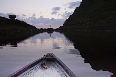 Österreich, Tirol, Fieberbrunn, Wildseeloder, Bug eines Bootes auf dem Wildsee mit Person am Seeufer in der Abenddämmerung - PSIF00071