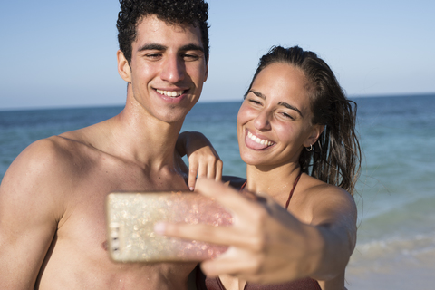 Glückliches junges Paar macht Selfies am Strand, lizenzfreies Stockfoto