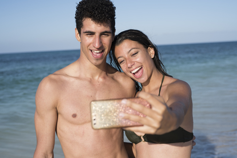Glückliches junges Paar macht Selfies am Strand, lizenzfreies Stockfoto
