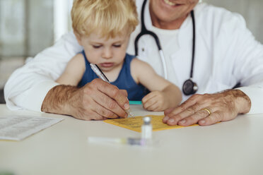 Toddler sitting on doctor's lap, while filling in immunization card - MFF04477