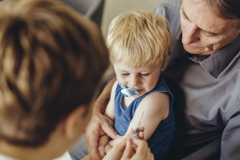 Vater hält seinen Sohn, während er von einem Kinderarzt geimpft wird, lizenzfreies Stockfoto