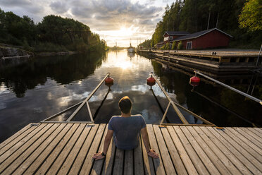 Finnland, Kajaani, Mann sitzt auf Steg und beobachtet Sonnenuntergang, Rückansicht - KKAF01708