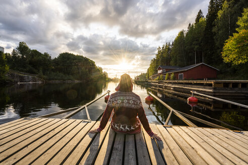 Finland, Kajaani, Man sitting on jetty, watching sunset, rear view - KKAF01710