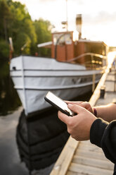 Finland, Kajaani, Man using smartphone at jetty, close-up - KKAF01713