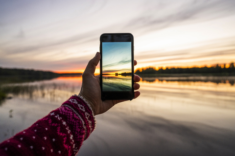 Finnland, Kajaani, Person, die ein Smartphone-Foto vom Sonnenuntergang macht, lizenzfreies Stockfoto