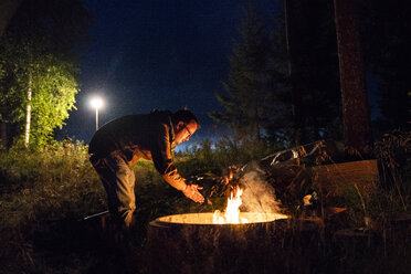 Finnland, Mann wärmt sich an einem Lagerfeuer auf einem Campingplatz - KKAF01727