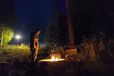 Finnland, Mann wärmt sich an einem Lagerfeuer auf einem Campingplatz - KKAF01728
