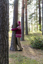 Finnland, Junger Mann umarmt Bäume in einem Wald - KKAF01734