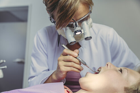 Denist examining boy's teeth, using head magnifiers and dental instrument - MFF04539