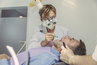 Patient getting dental treatment, dentist using dental drill and head magnifiers and light - MFF04546