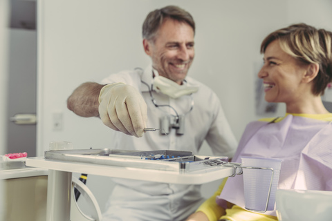 Zahnarzt, der die Instrumente nach der Behandlung auf das Tablett legt und seinen lächelnden Patienten ansieht, lizenzfreies Stockfoto