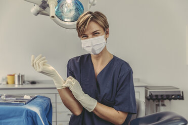 Dental surgeon wearing surgical mask, putting on surgical gloves - MFF04580