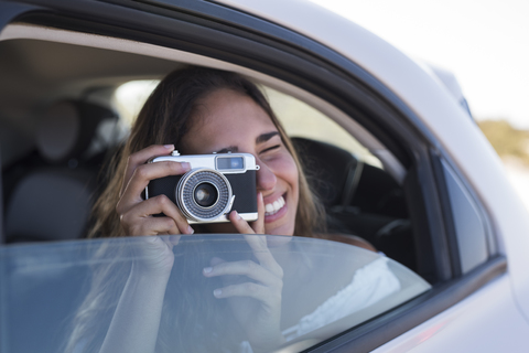 Frau sitzt im Auto und fotografiert mit einer Kamera, lizenzfreies Stockfoto