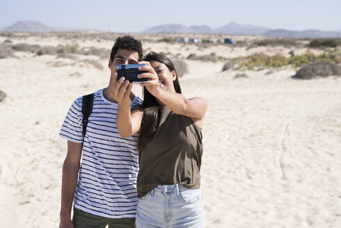 Junges Paar, das sich am Strand amüsiert und mit dem Smartphone Selfies macht - PACF00108