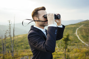 Businessman looking through binoculars on top of a mountain - BSZF00581