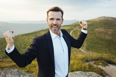 Portrait of self-confident businessman standing on top of a mountain - BSZF00583
