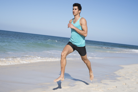 Spanien, Kanarische Inseln, Fuerteventura, junger Mann läuft am Strand, lizenzfreies Stockfoto