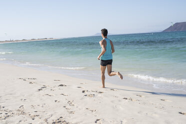 Spanien, Kanarische Inseln, Fuerteventura, Rückansicht eines jungen Mannes beim Laufen am Strand - PACF00136