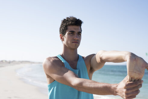 Spanien, Kanarische Inseln, Fuerteventura, junger Mann streckt seinen Arm am Strand aus - PACF00139