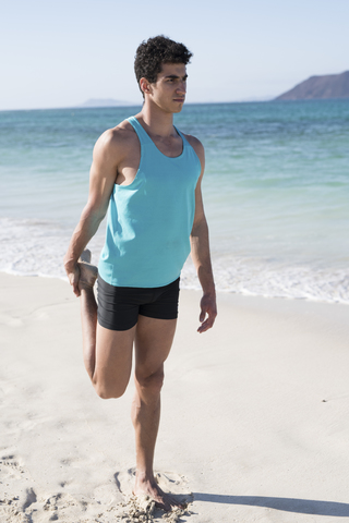 Spanien, Kanarische Inseln, Fuerteventura, junger Mann streckt sein Bein am Strand, lizenzfreies Stockfoto