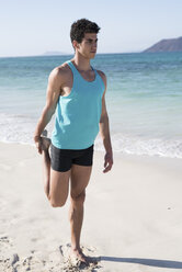 Spain, Canary Islands, Fuerteventura, young man stretching his leg on the beach - PACF00140