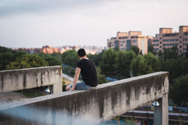 Back view of man sitting on a wall enjoying view at evening light - KKAF01760