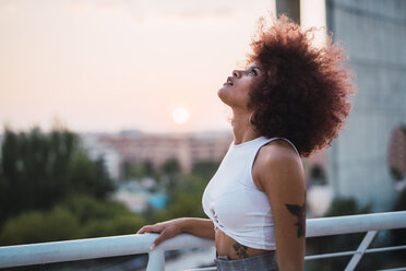 Porträt einer jungen Frau auf einer Terrasse in der Abenddämmerung mit Blick nach oben - KKAF01765