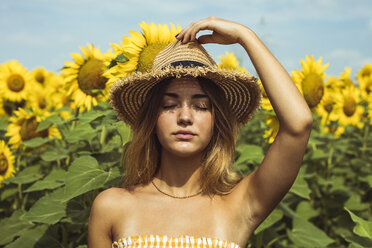 Young woman holding a straw hat on her head in a field of sunflowers - ACPF00325