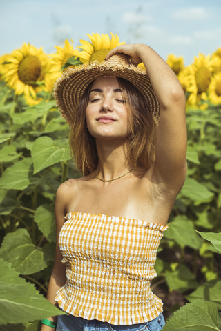 Junge Frau mit einem Strohhut auf dem Kopf in einem Sonnenblumenfeld, lizenzfreies Stockfoto