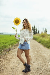 Junge Frau auf einem Feldweg mit einer Sonnenblume in der Hand - ACPF00334
