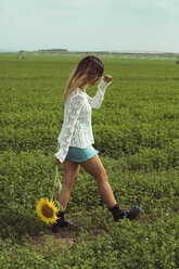 Junge Frau, die eine Sonnenblume auf einer grünen Wiese hält - ACPF00336
