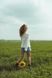 Junge Frau, die eine Sonnenblume auf einer grünen Wiese hält - ACPF00337