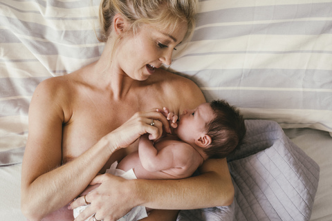 Mutter spricht mit ihrem neugeborenen Baby, das Haut an Haut im Bett liegt, lizenzfreies Stockfoto