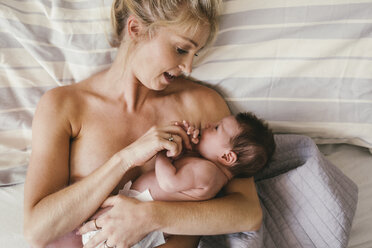 Mutter spricht mit ihrem neugeborenen Baby, das Haut an Haut im Bett liegt - MFF04587