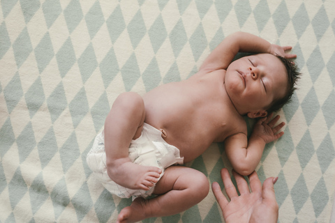Mutterhand und neugeborener Junge in Windeln auf einer Decke liegend, lizenzfreies Stockfoto