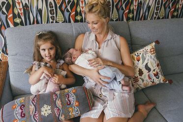 Lächelnde Mutter sitzt mit neugeborenem Baby und Tochter auf der Couch - MFF04598