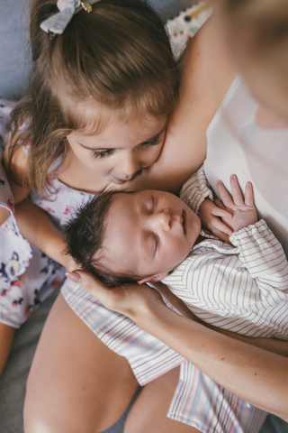 Mother holding her baby close with sister looking at him stock photo