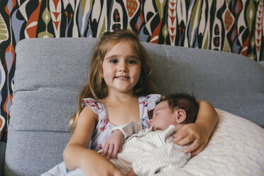 Lächelndes Mädchen sitzt auf der Couch und hält ihren neugeborenen kleinen Bruder - MFF04606