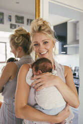 Portrait of happy mother holding her baby close in front of mirror at home - MFF04610