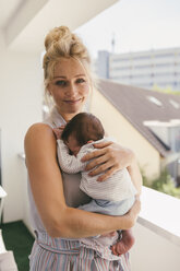 Portrait of smiling mother holding her baby on balcony - MFF04613