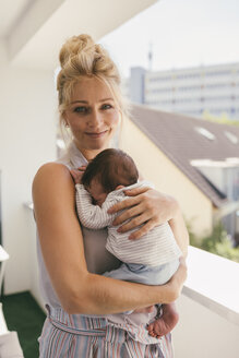 Porträt einer lächelnden Mutter, die ihr Baby auf dem Balkon hält - MFF04613