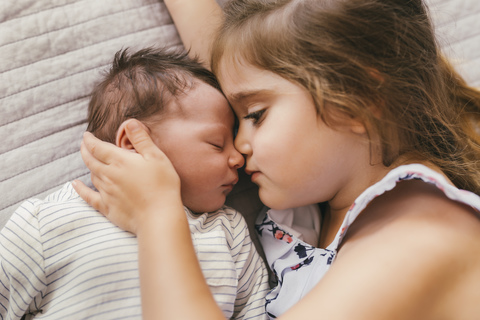 Liebevolles Mädchen, das auf einer Decke liegt und mit ihrem kleinen Bruder kuschelt, lizenzfreies Stockfoto