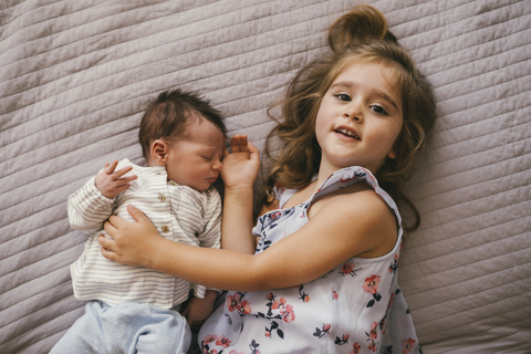 Smiling girl lying on blanket cuddling with her baby brother stock photo