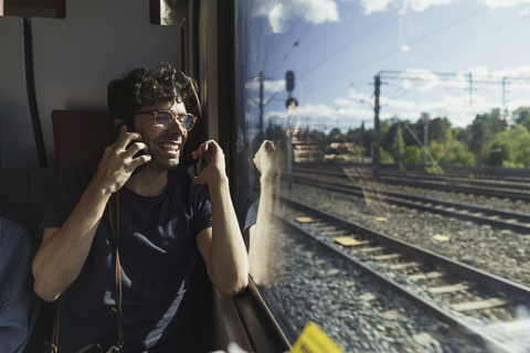 Glücklicher Mann, der mit dem Zug reist und mit seinem Handy telefoniert, lizenzfreies Stockfoto