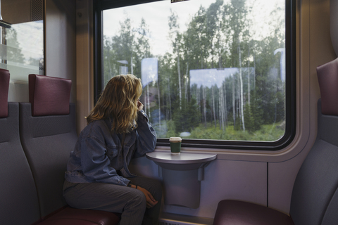 Frau reist mit dem Zug und schaut aus dem Fenster, lizenzfreies Stockfoto