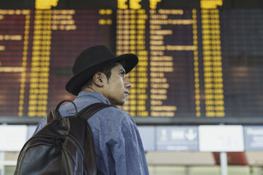 Junger Mann mit Hut und Rucksack an der Abflugtafel auf dem Flughafen - KKAF01791