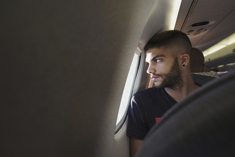 Junger Mann in einem Flugzeug schaut aus dem Fenster, lizenzfreies Stockfoto